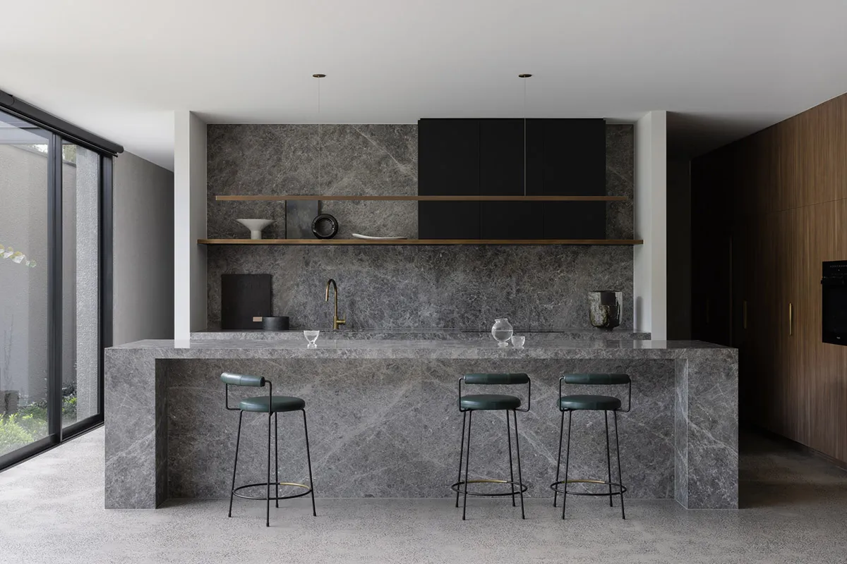 A modern kitchen with a marble countertop, bar stools, and dark cabinets.