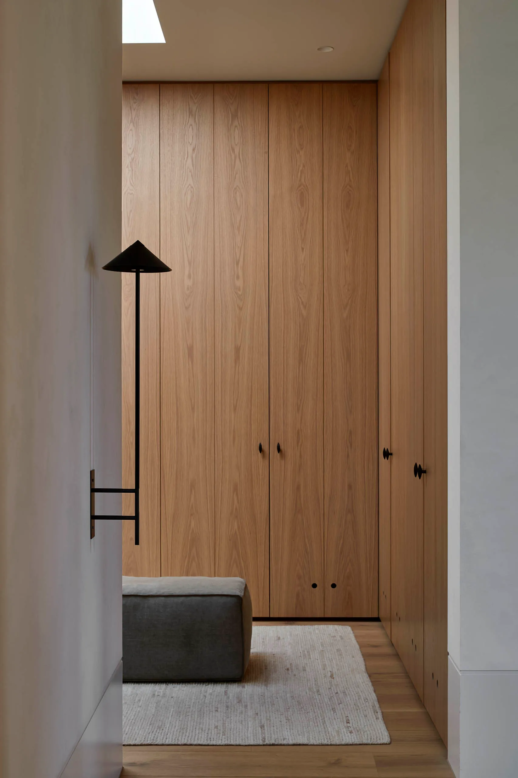 Modern minimalist closet with wood panels and a small ottoman on a white rug.