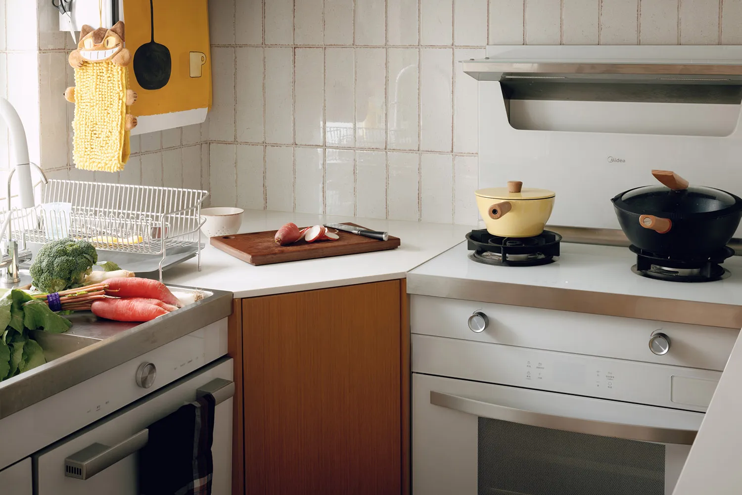 A modern minimalist kitchen with white tiles, stainless steel appliances, and wooden elements.