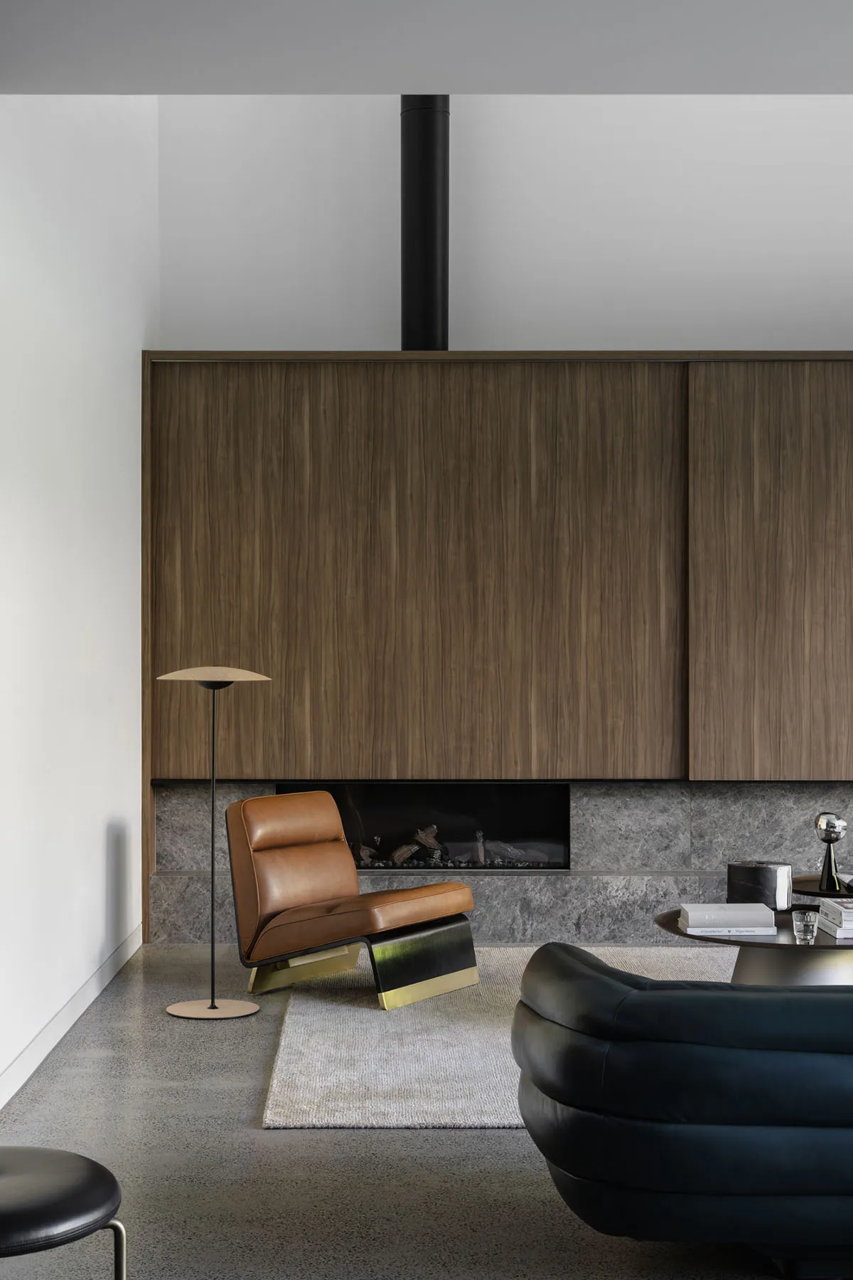 Modern minimalist living room featuring a brown leather lounge chair, black marble coffee table, and wooden cabinets in marbl