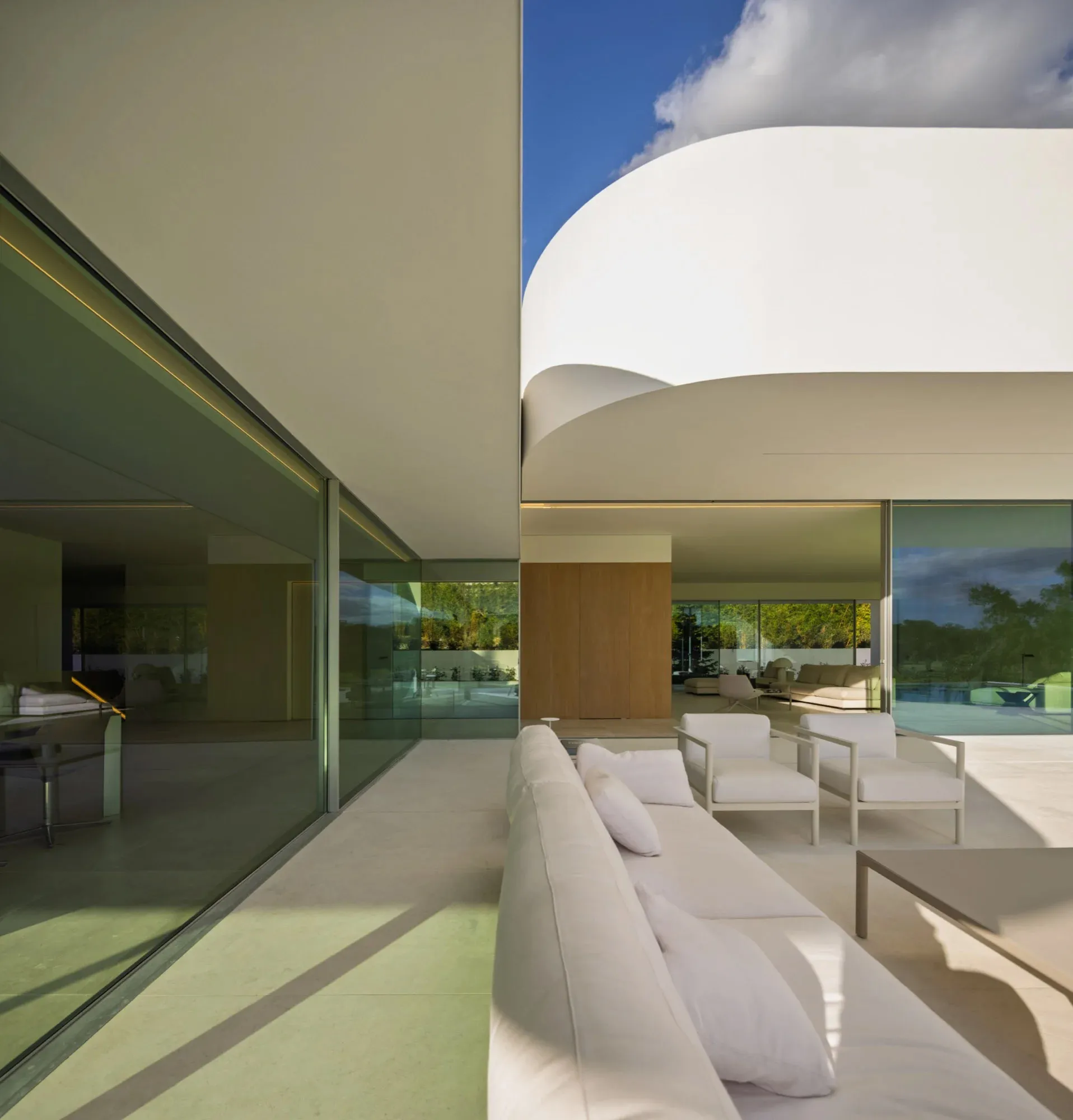 Modern minimalist residential interior with glass walls, concrete floors, and wooden accents.