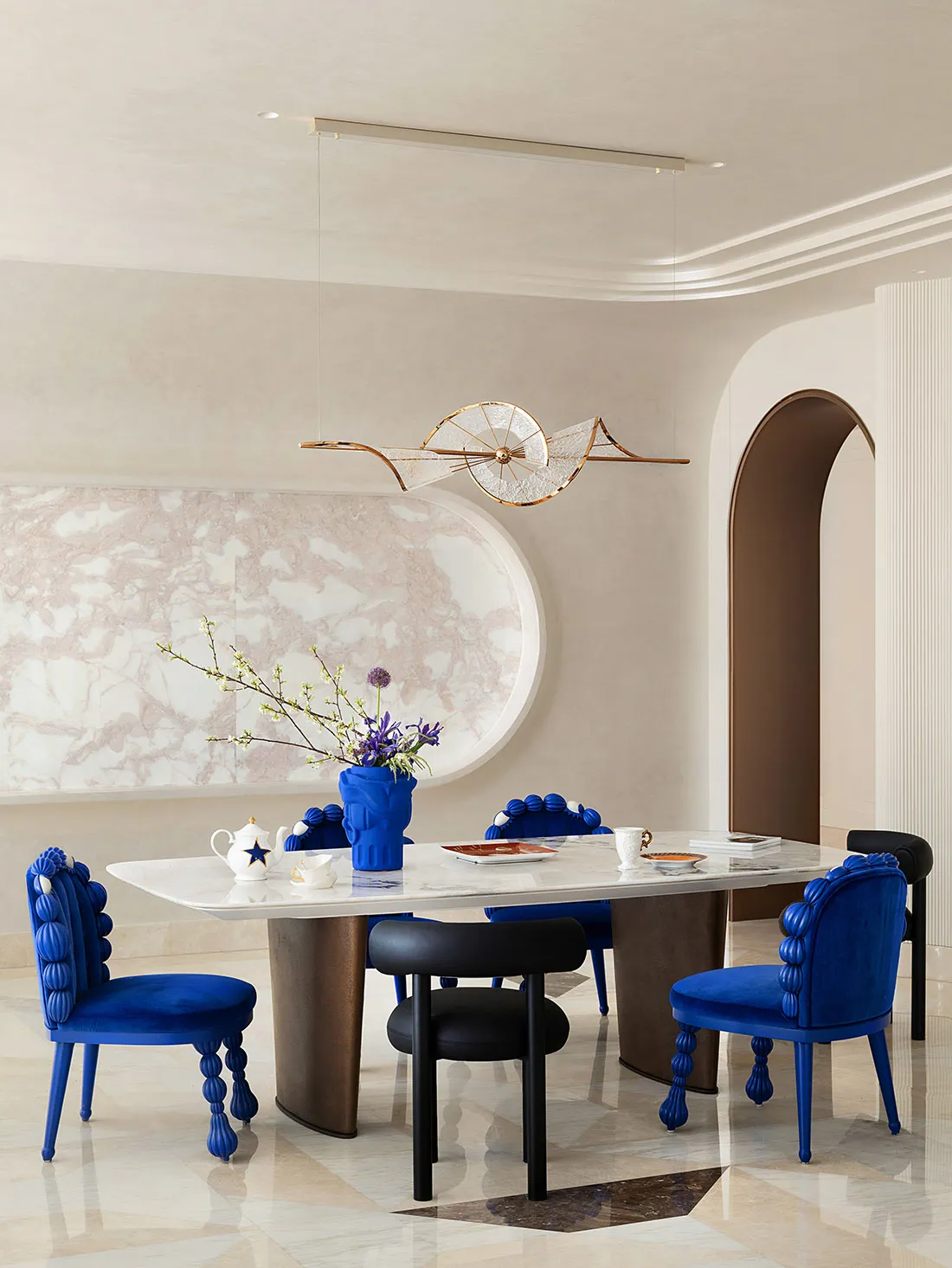 Modern dining room with a marble table, blue velvet chairs, and decorative lighting.
