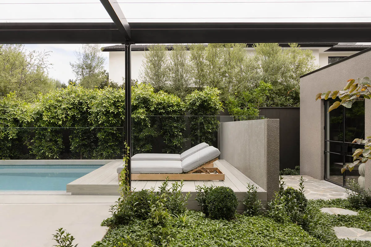 Modern minimalist outdoor space featuring a walkout patio, pergola, and pool surrounded by lush greenery and minimalist furni