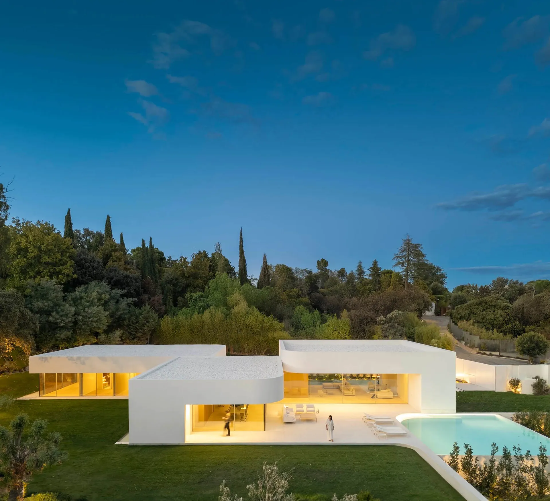 A modern minimalist villa with concrete and glass walls and a swimming pool in the foreground and mountains in the background