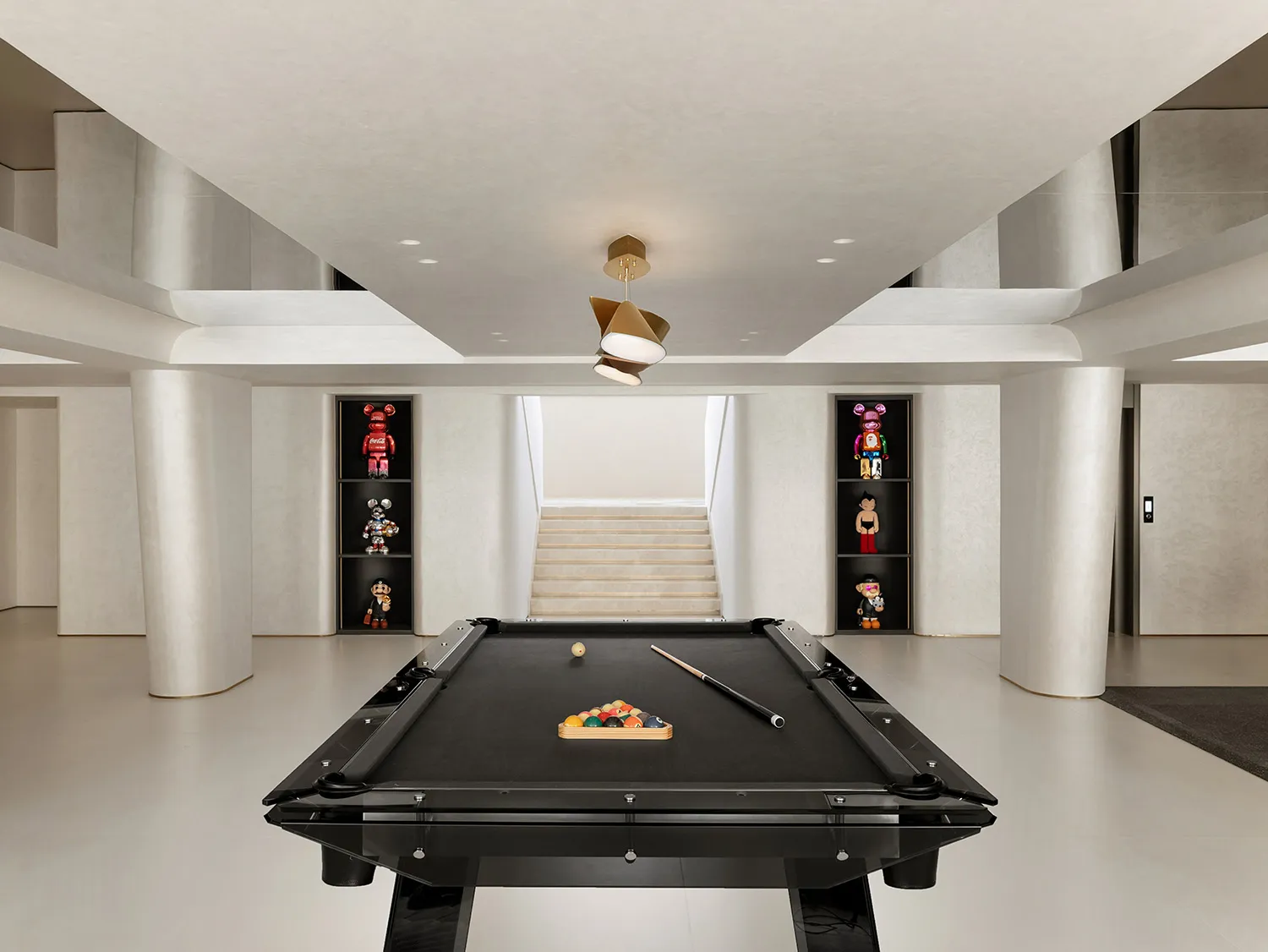 A minimalist playroom featuring a black pool table with billiard balls and cues, surrounded by concrete pillars and shelves d