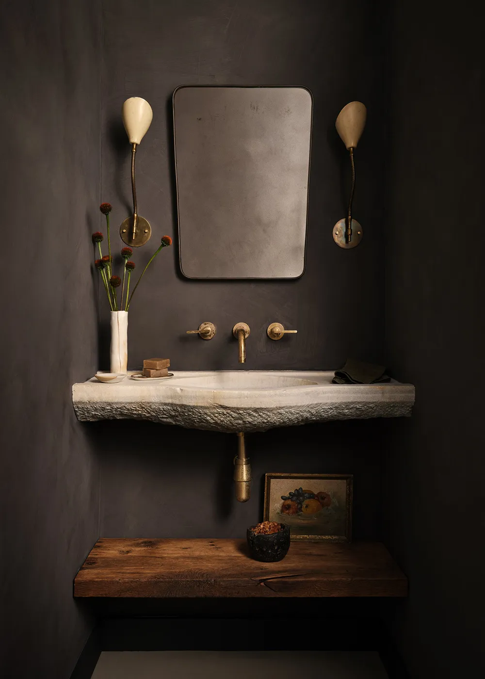 A minimalist bathroom with a concrete sink, brass fixtures, and dark walls.