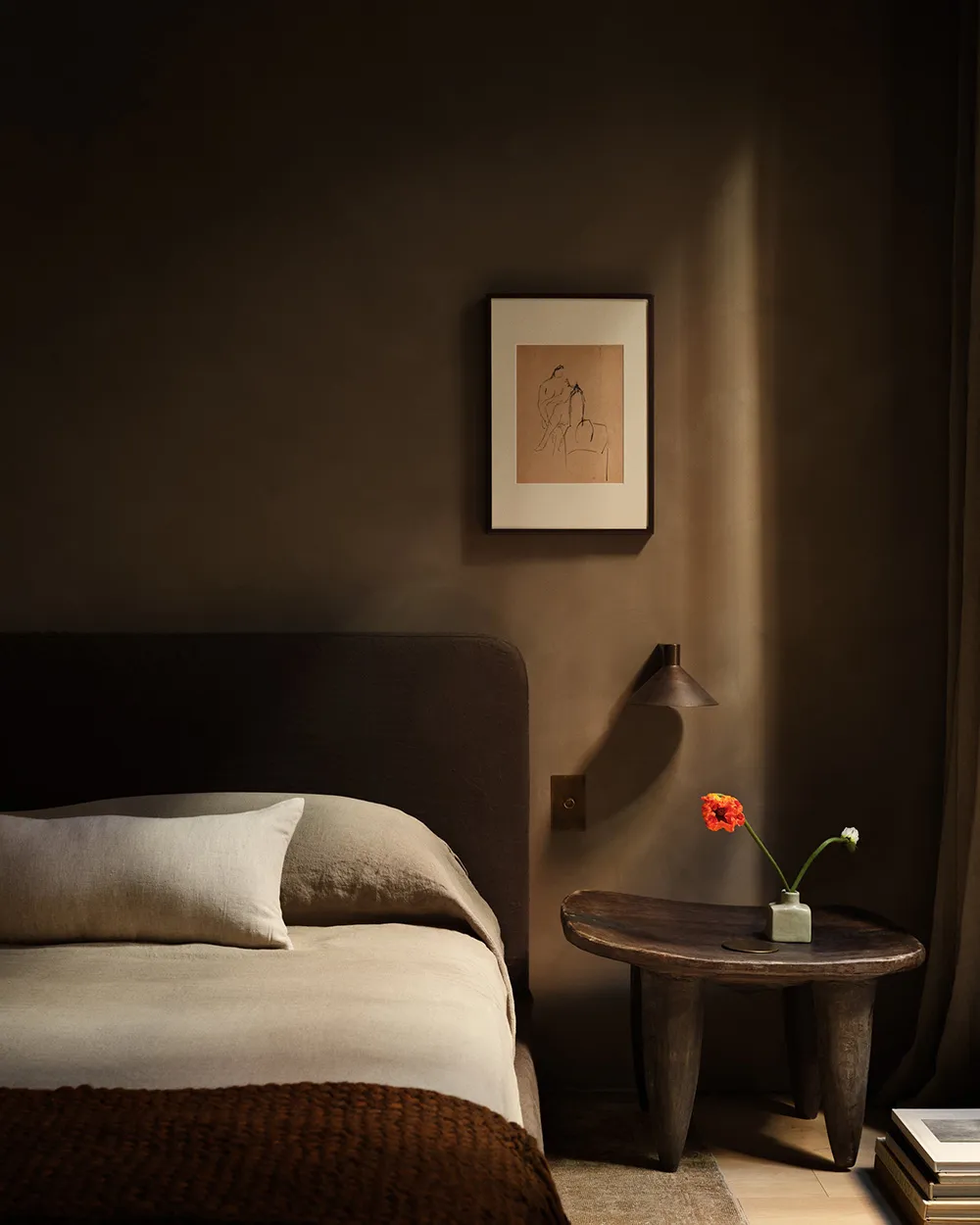 A minimalist bedroom featuring a bed with a beige comforter and white pillows, a wooden bedside table with a vase of flowers,