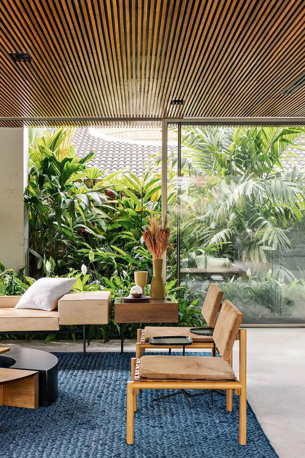 A modern interior living room with wooden furniture, plants, and a blue rug.