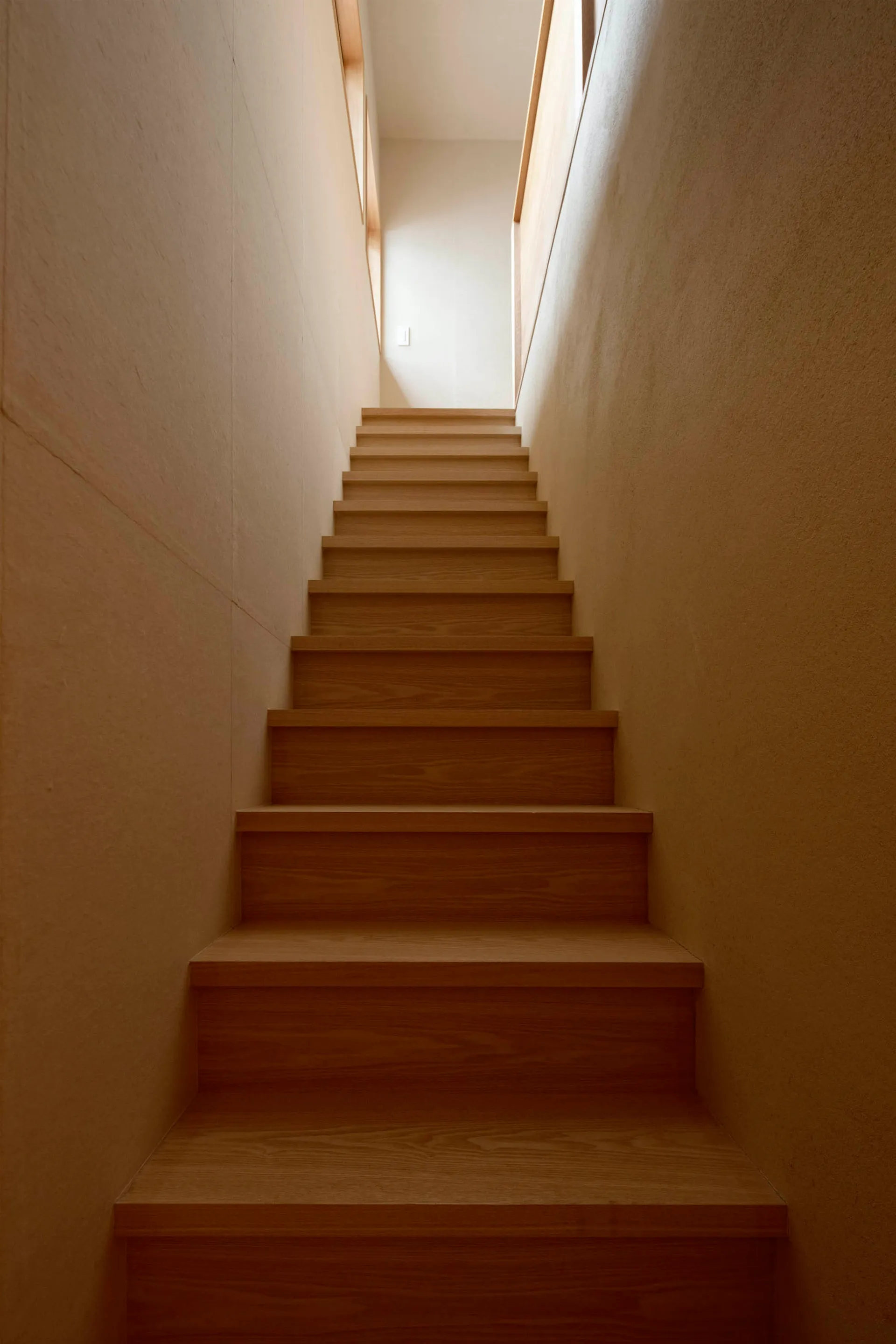 Modern minimalist wooden stairs leading upwards to a light-filled space.