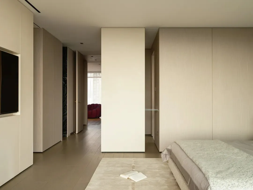 Modern bedroom with textured beige walls and wood floor, featuring a bed with beige and white bedding.