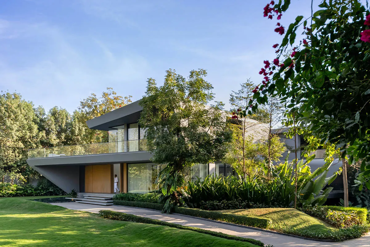 A modern house with concrete and glass features, surrounded by a lush green garden.