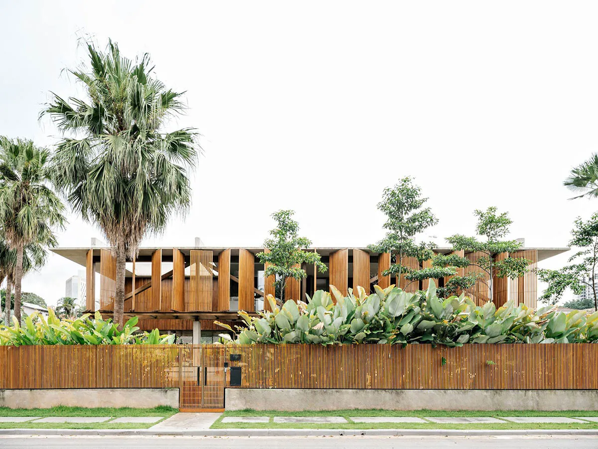 Modern residential house with wooden exterior, surrounded by plants and palm trees.