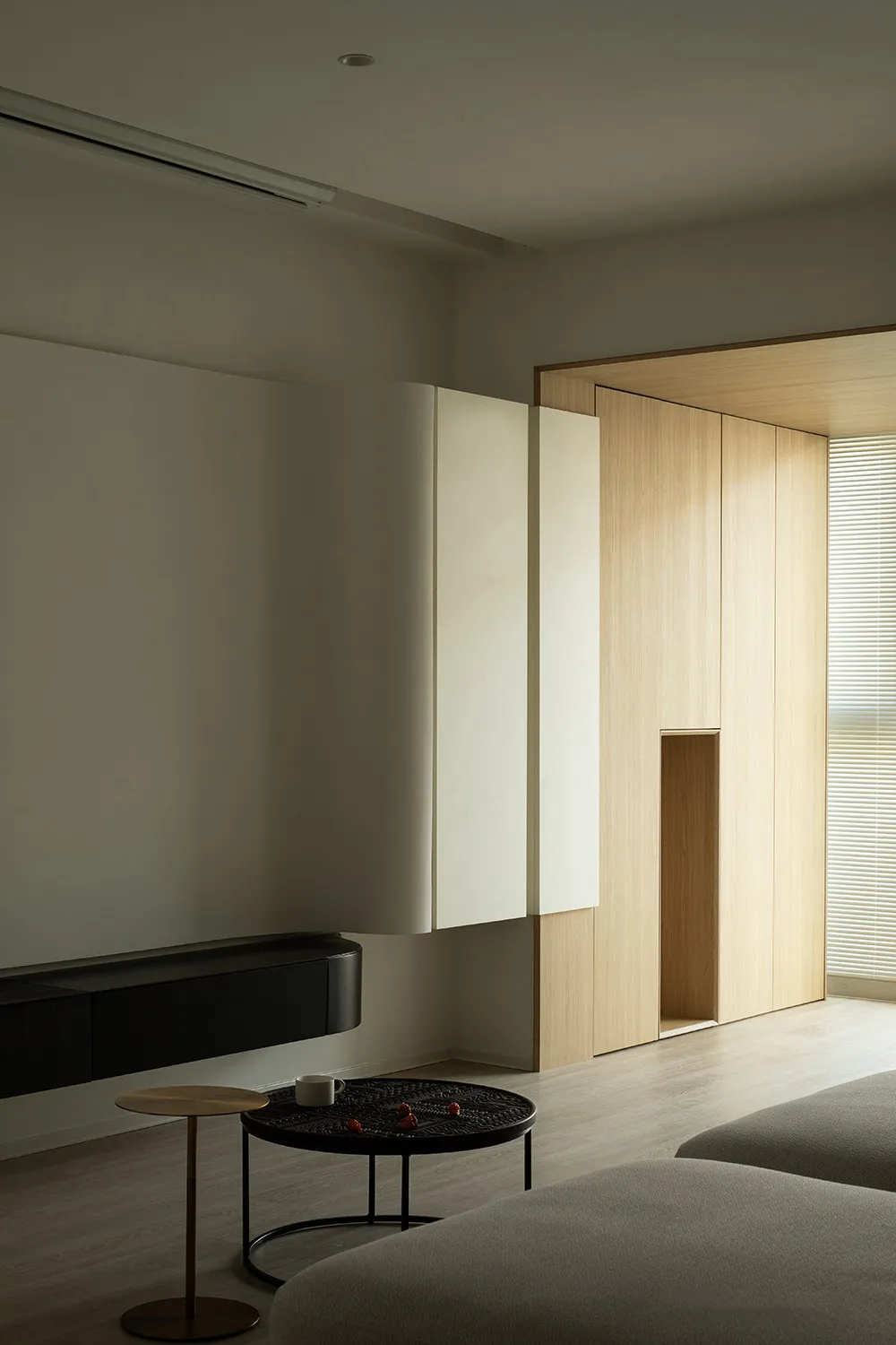 A minimalist living room featuring wooden furniture, glass walls, and concrete surfaces.
