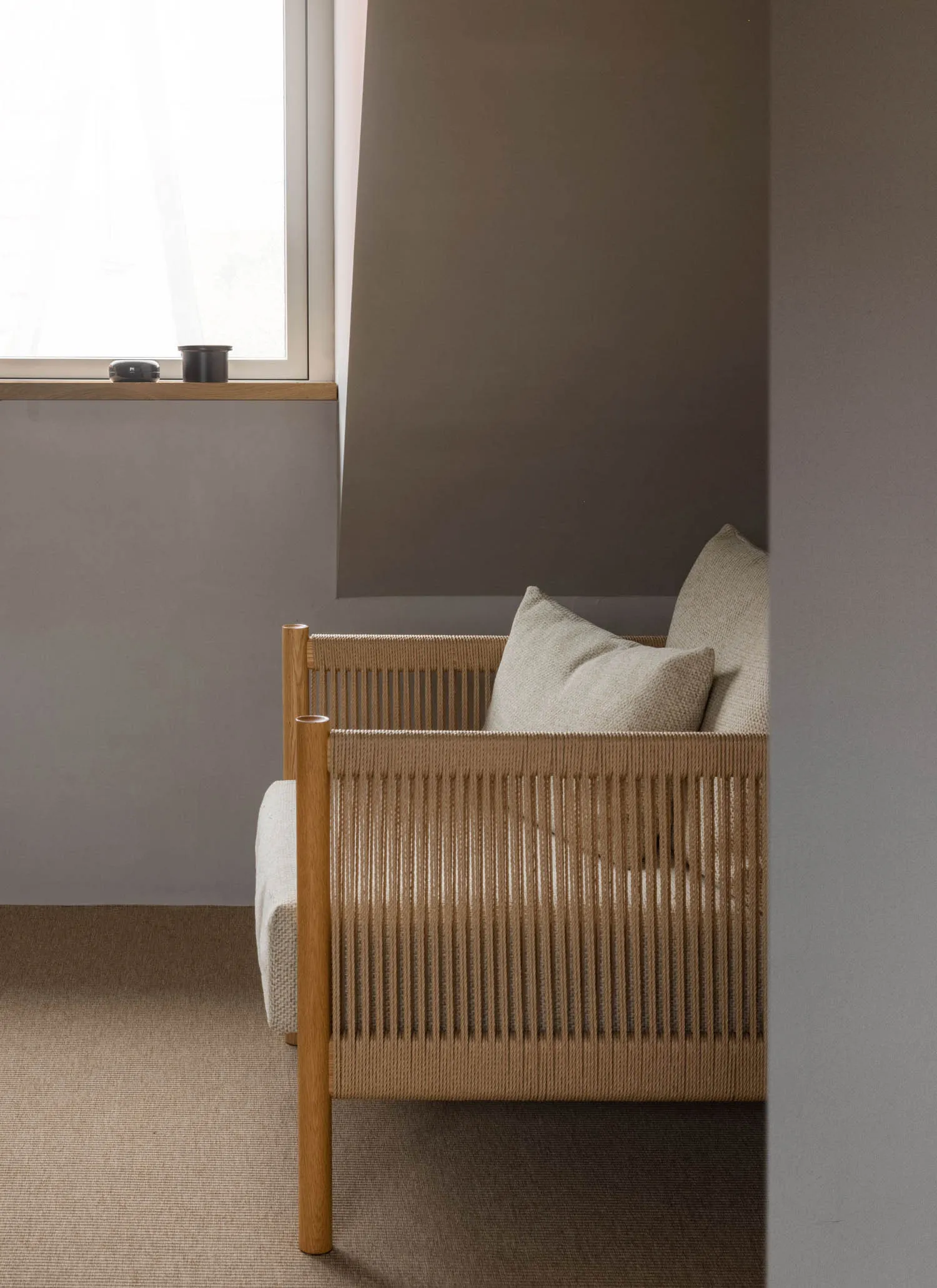 A minimalist residential space featuring a wooden chair and fabric cushions with a window on a grey wall.
