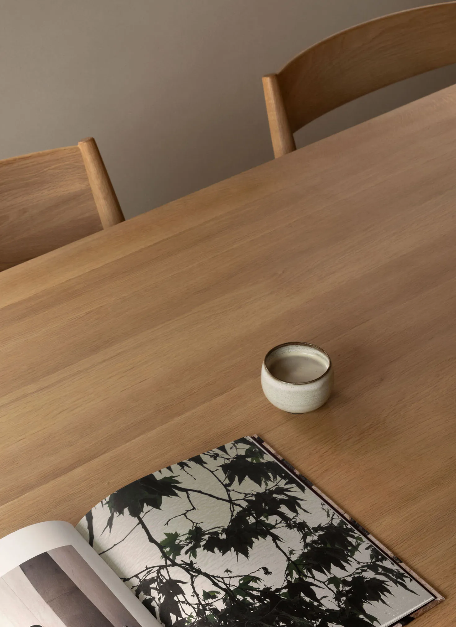 A wooden dining table with chairs, a small ceramic cup, and an open book with a botanical image.