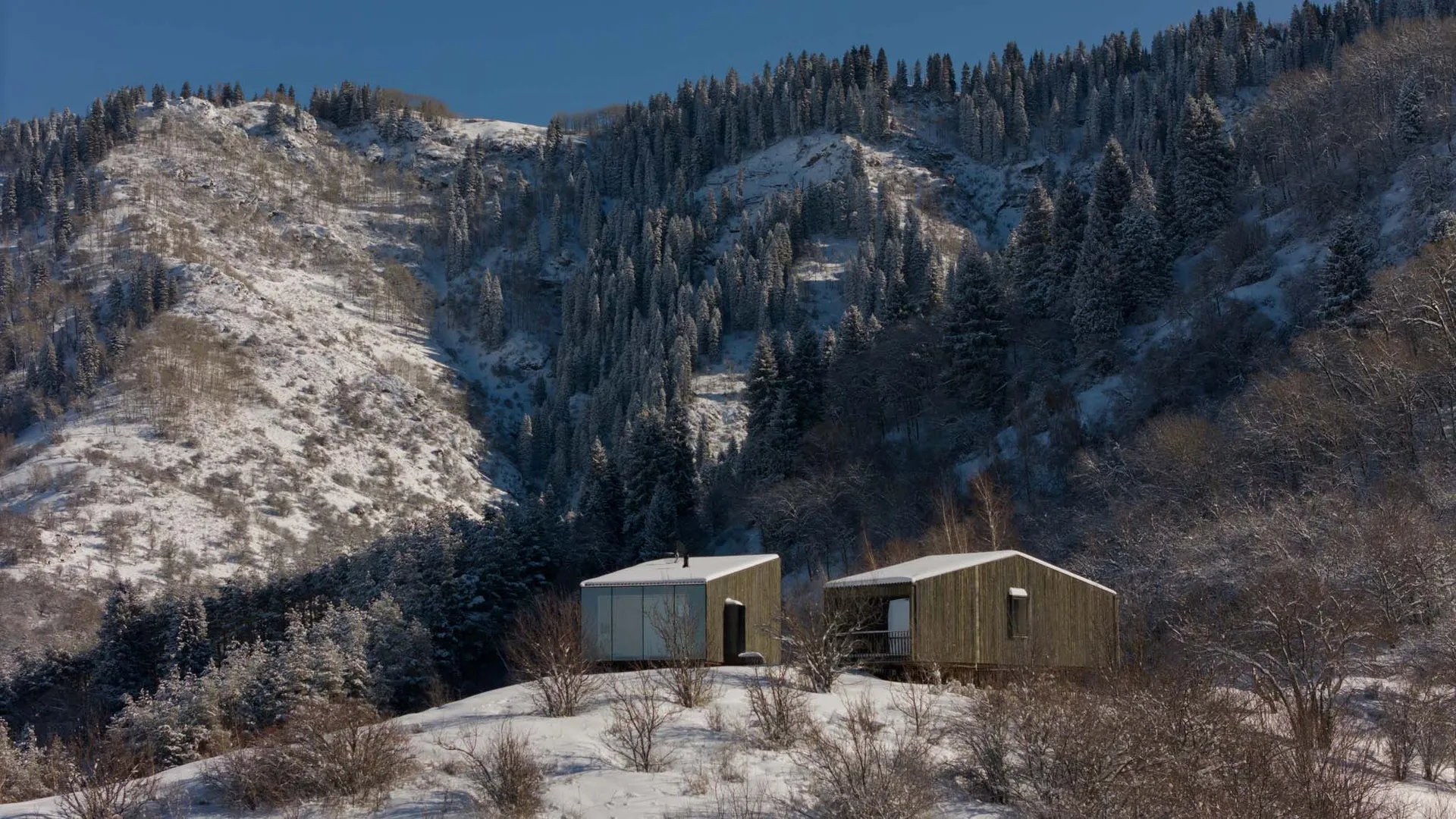 一棟擁有木質外觀的現代住宅，靜靜坐落在覆雪的山坡上。