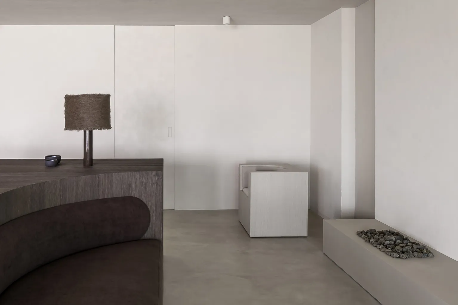 A modern minimalist interior space featuring concrete elements, a wooden sofa, a lamp, and a stone feature wall.