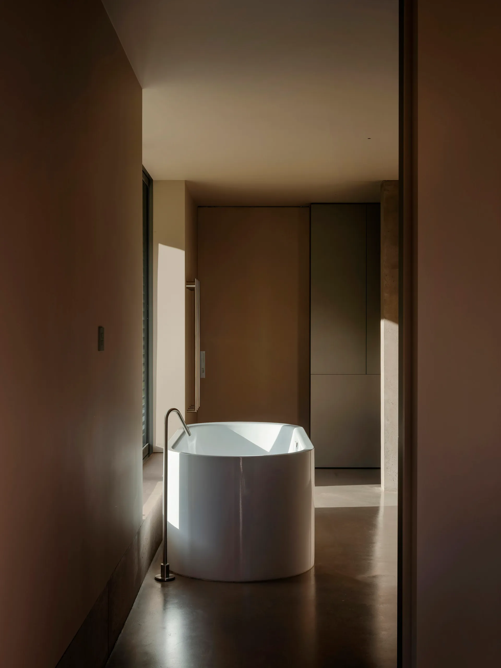 A minimalist white bathroom with a cylindrical ceramic soaking tub placed in the corner.