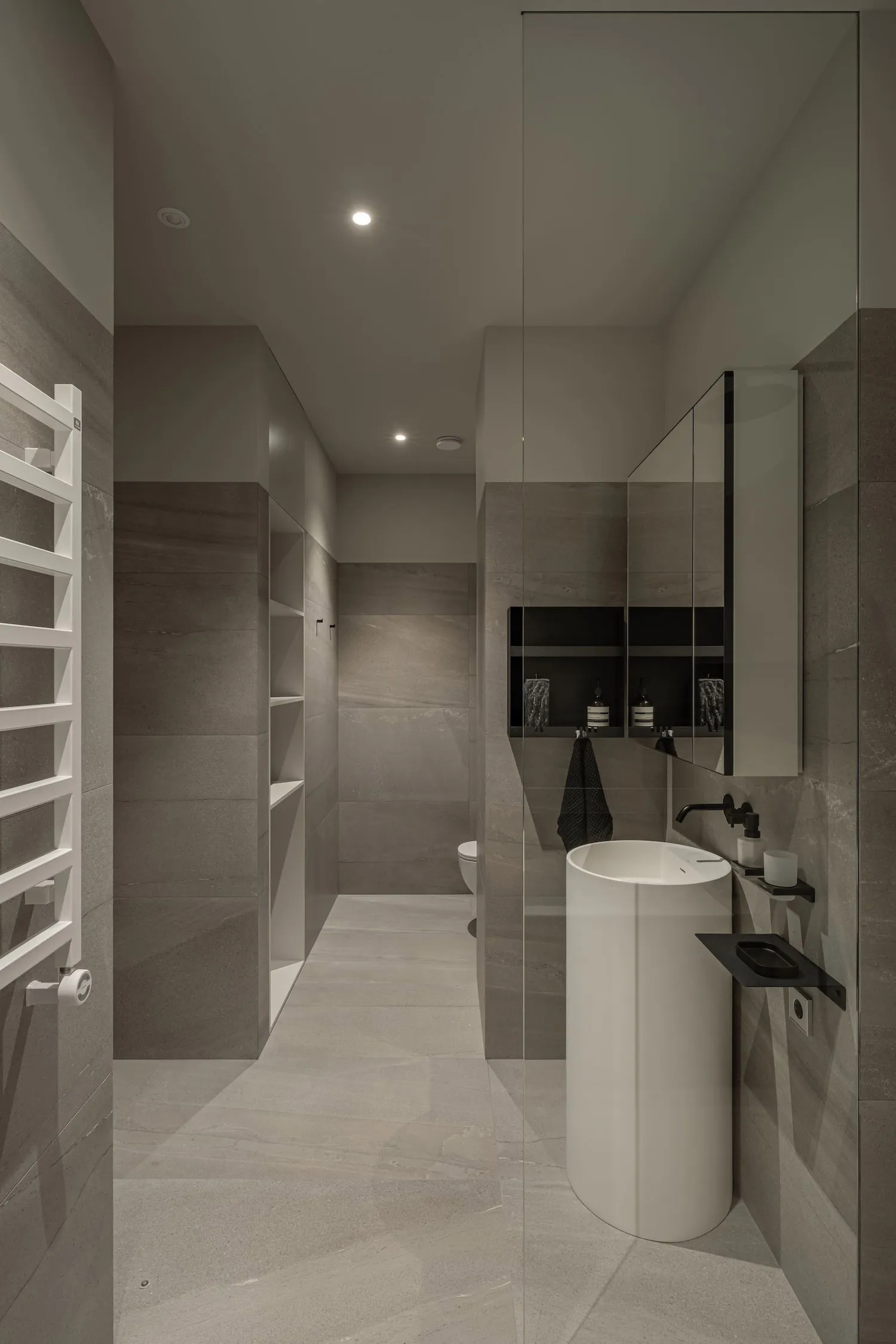 A modern minimalist bathroom with concrete tiles, featuring a sleek white pedestal sink, a large mirror, and plenty of storag