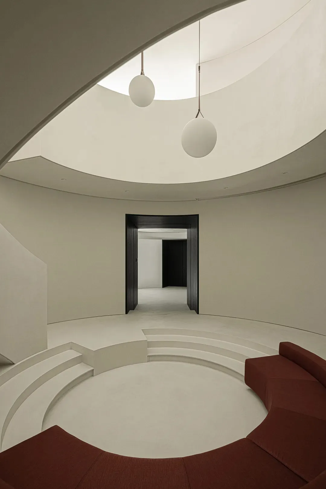 A minimalist living room with a circular seating area, white concrete steps, a red fabric seating area, and two hanging round
