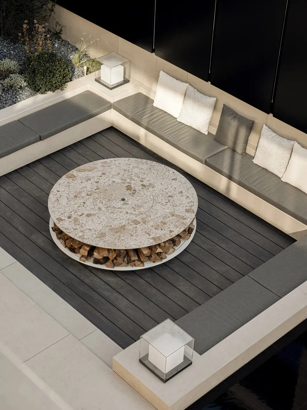 Modern patio furniture set with a round marble table and built-in seating made of concrete, surrounded by a landscaped area w