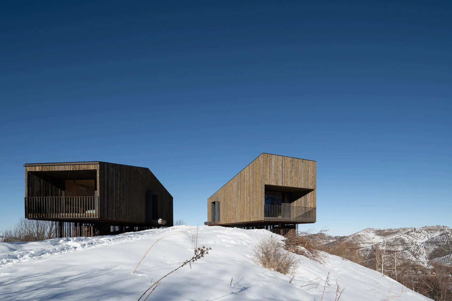 Two modern residences with wooden cladding situated on a snowy hillside