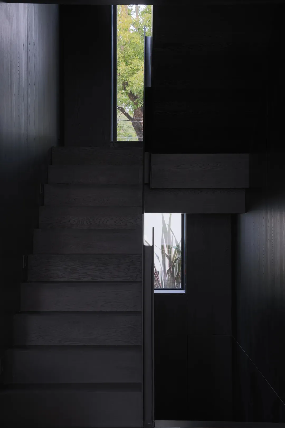 A modern black staircase with wooden steps in a dark interior space.