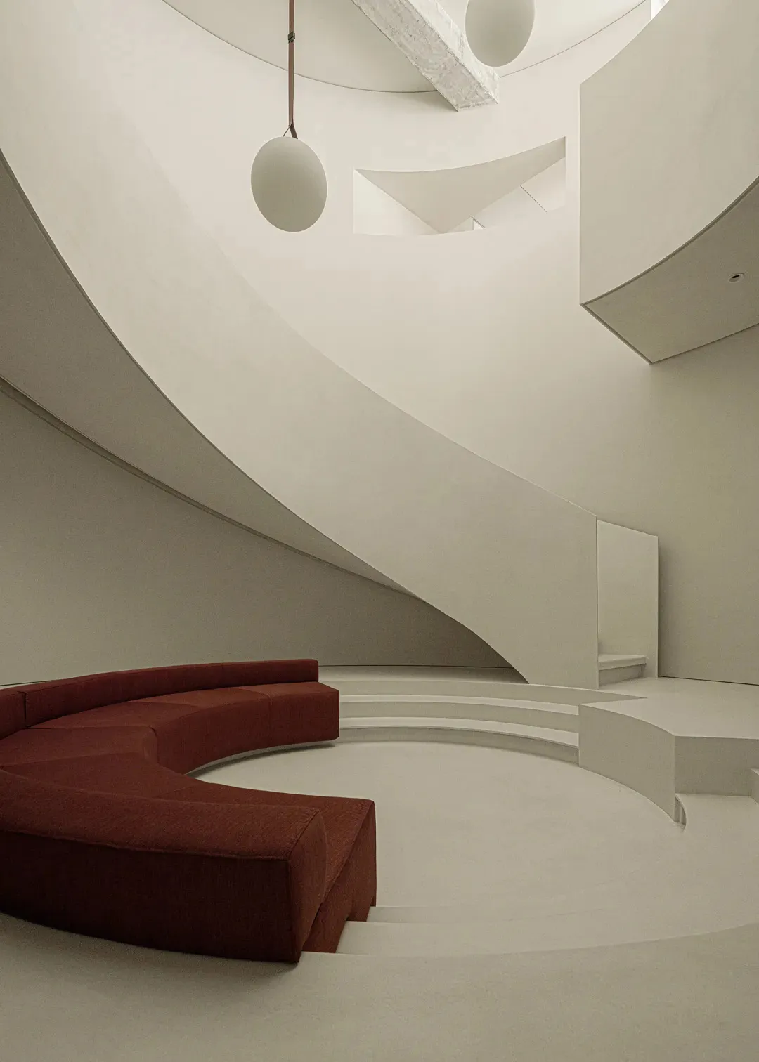 A modern interior space with curved concrete walls and a red sofa.