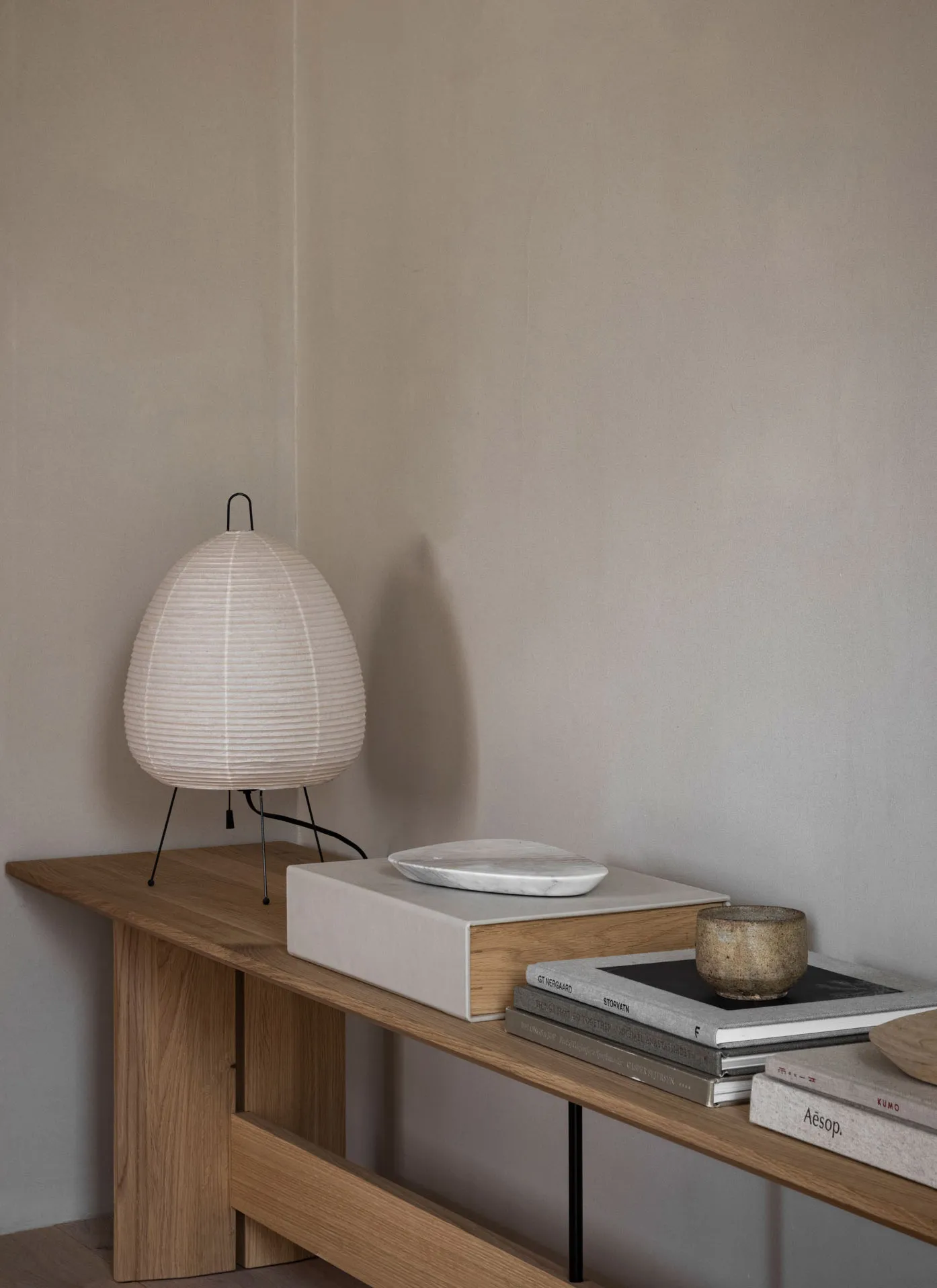 A modern living room with a wooden table, a white lampshade, and some books on a wooden shelf.