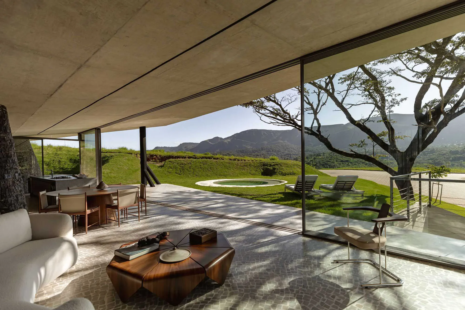 A modern residential interior with a concrete ceiling and floor, featuring a spacious living area with a round wooden coffee