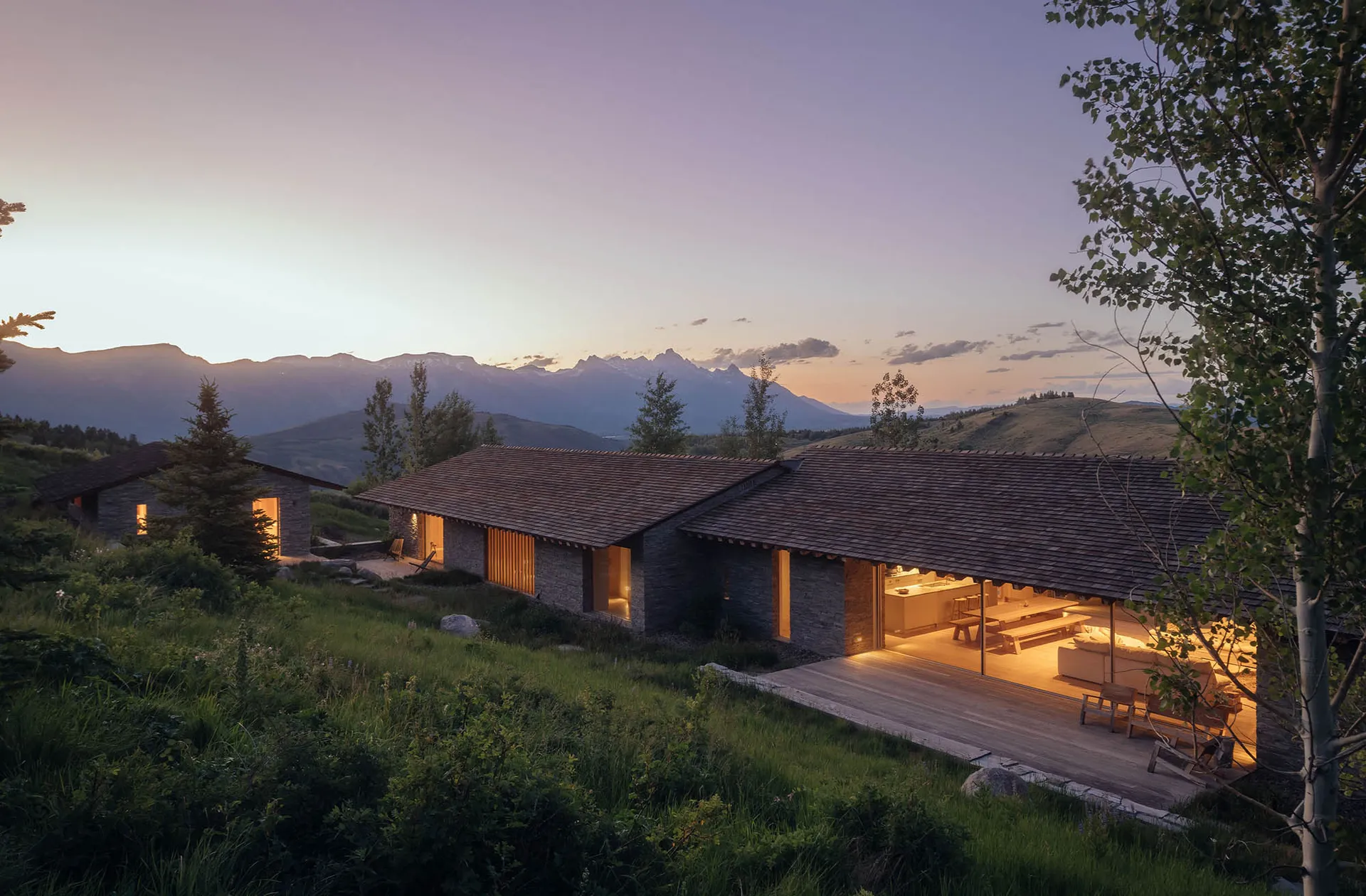 A modern residential exterior with stone walls and a wooden roof at dusk.