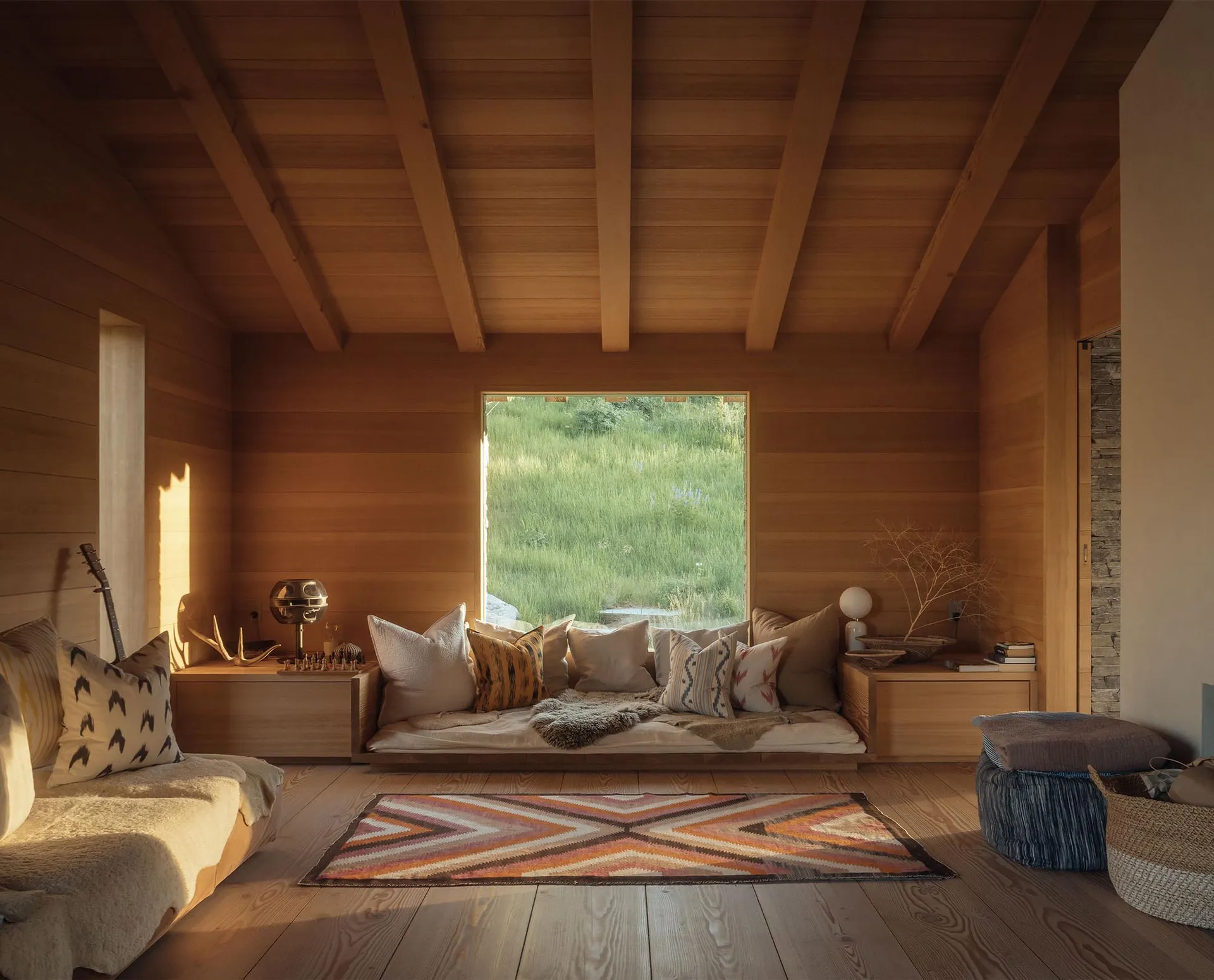 A cozy, modern residential interior with wooden walls, floors, and ceiling beams, featuring a couch with colorful cushions an