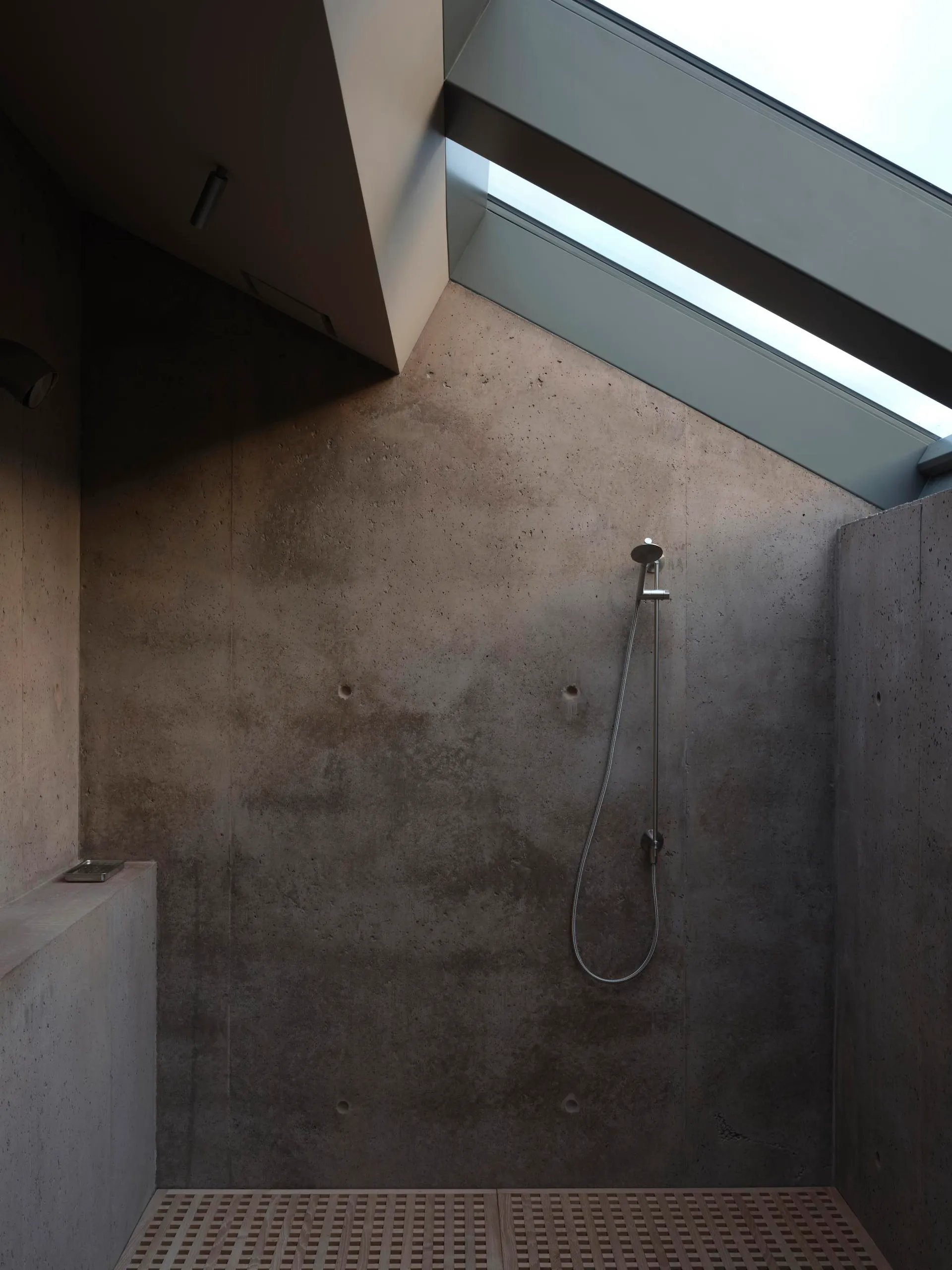 Bathroom with concrete walls, ceiling, and floor, featuring a minimalistic design with a shower head and skylight.