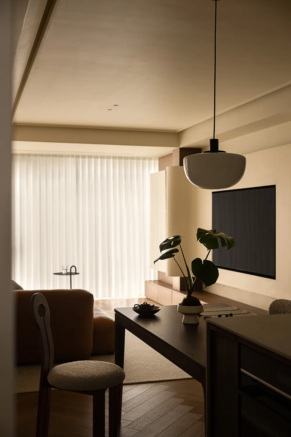 A minimalist living room with wooden flooring, featuring a modern sofa, a coffee table with a glass vase, and a large window