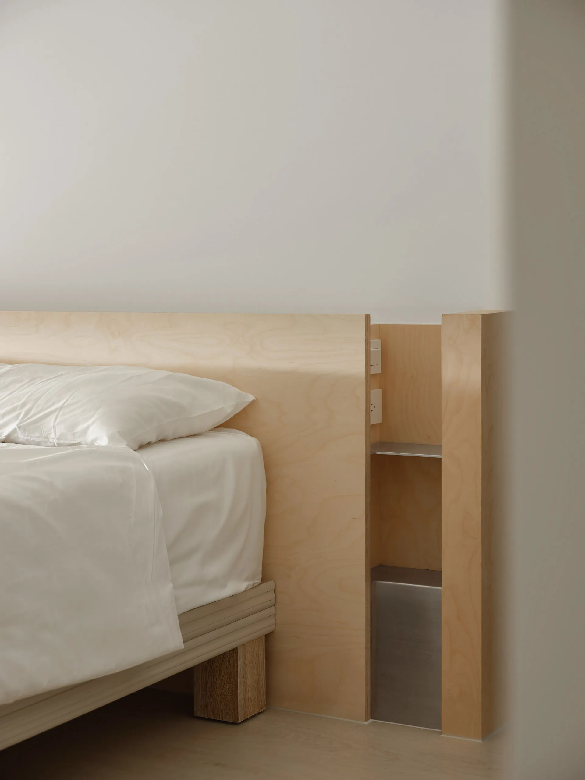 A modern minimalist bedroom with a white bed and white bedding, featuring a natural wood headboard and minimalist wooden furn