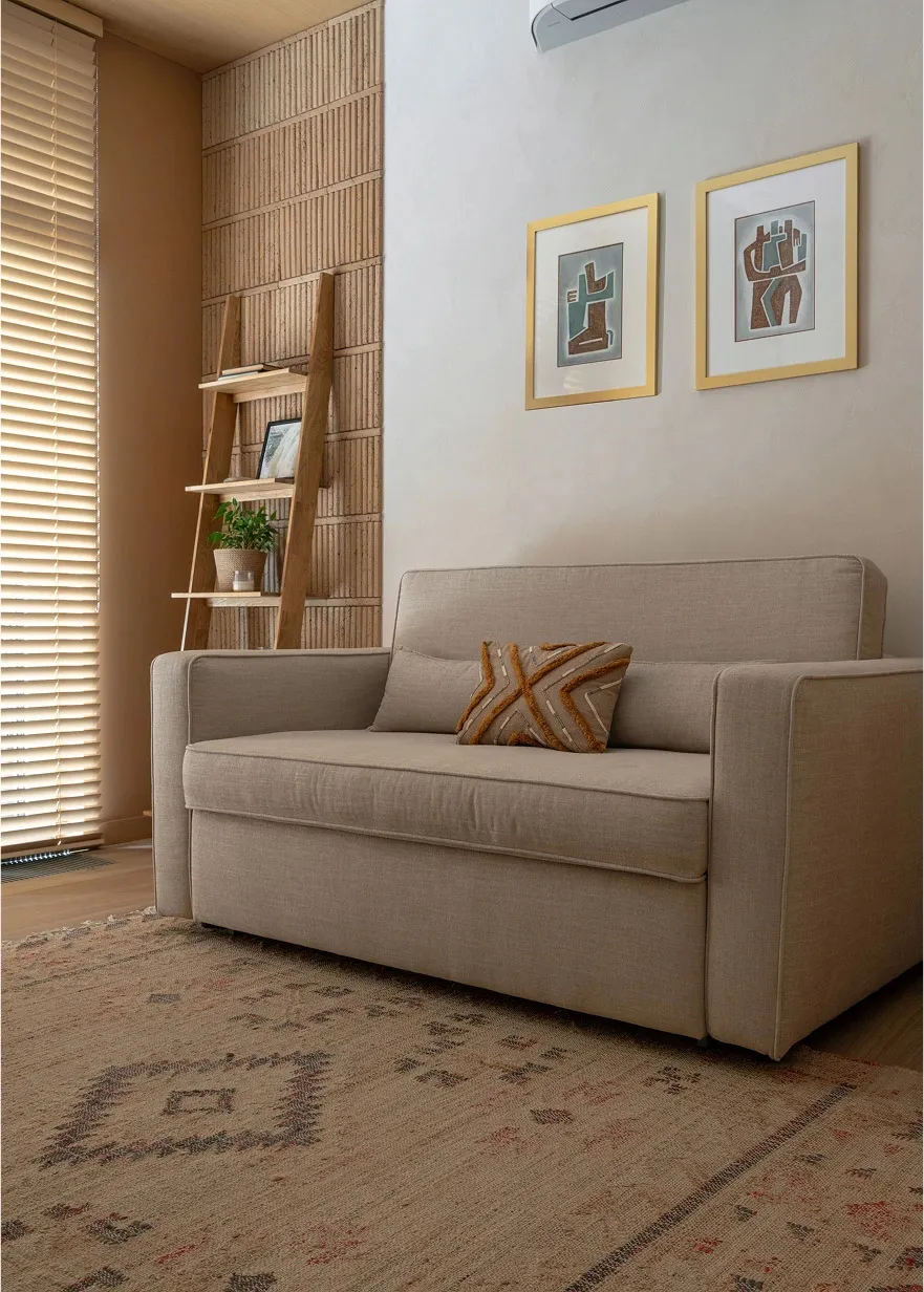 Modern minimalist living room with a beige fabric sofa, framed artwork, and a wooden ladder-style bookshelf.