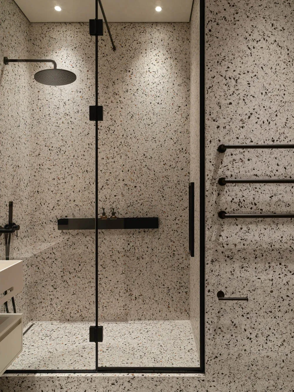 A modern bathroom featuring white terrazzo flooring and walls with black speckles, and minimal black fixtures