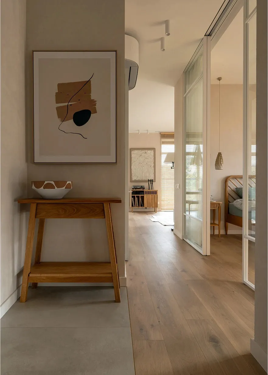 Modern minimalist entryway featuring a wooden console table, abstract artwork, and wooden flooring.