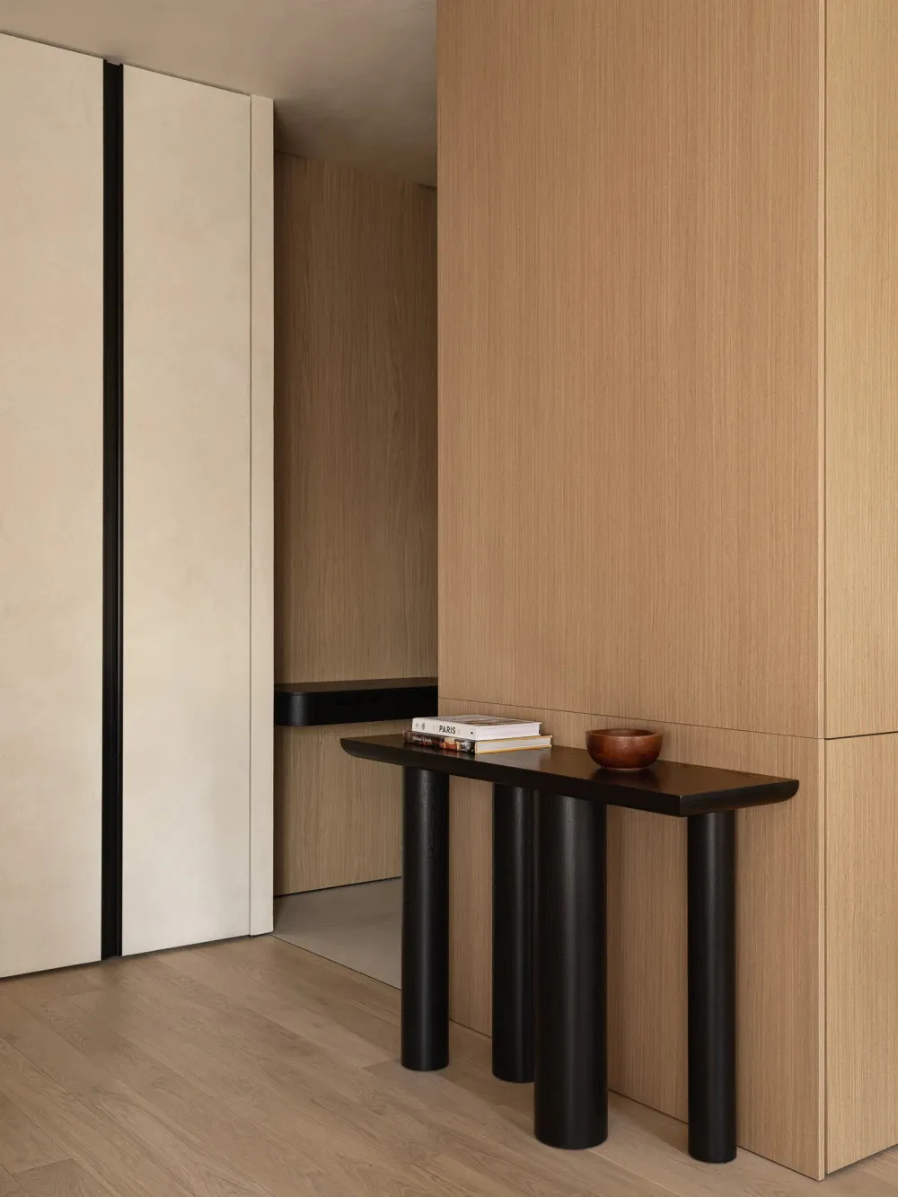 Modern indoor console table with wood surface and black cylindrical legs, positioned in a minimalist room with wooden walls a