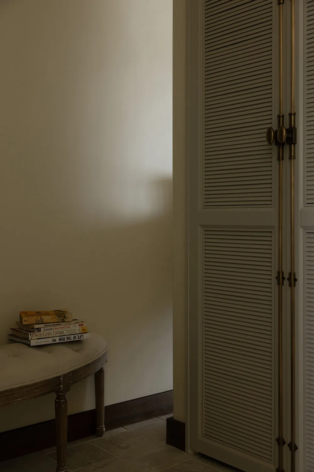 A minimalist bedroom featuring taupe-colored furniture and a neatly stacked pile of books on a round ottoman.