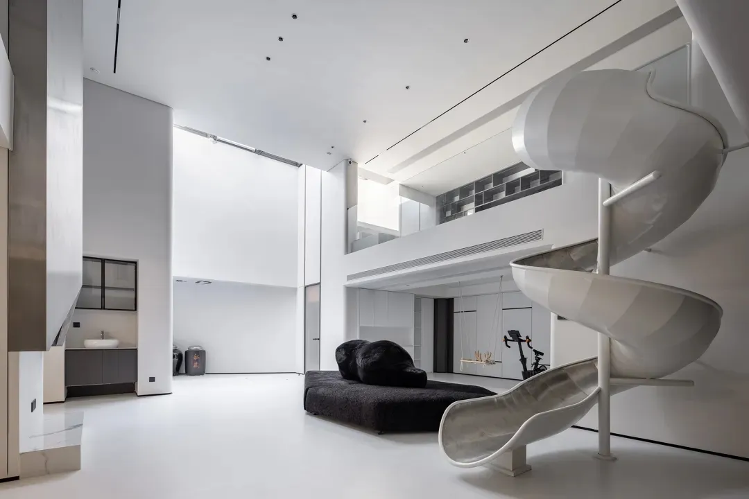 A minimalist, all-white residential interior featuring a spiral slide and black bean bag chairs.