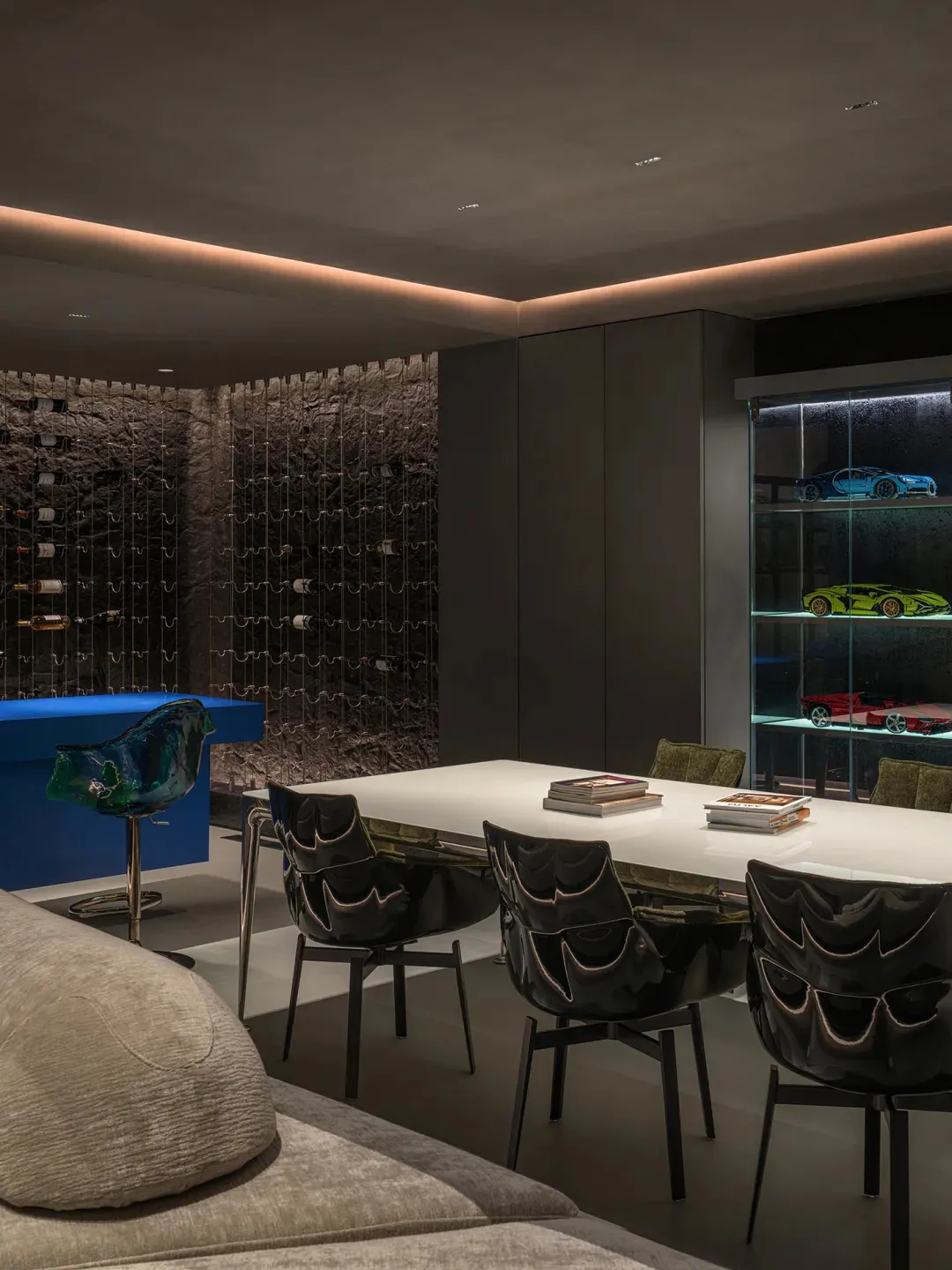 Modern minimalist meeting room with metallic and glass elements, featuring a white table, black chairs, and a blue bar stool.