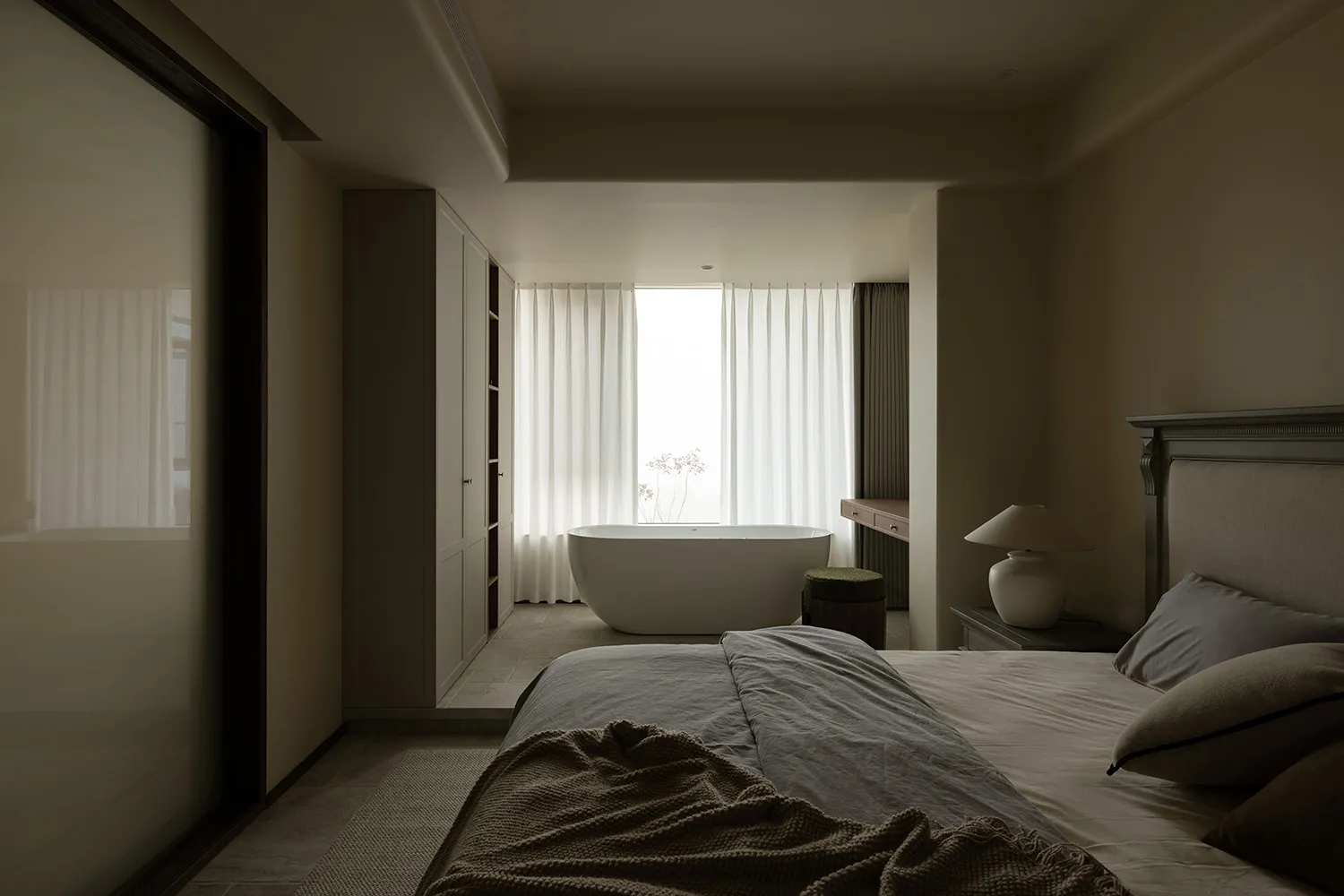 A minimalist bedroom features a concrete floor and a freestanding bathtub with sheer curtains.