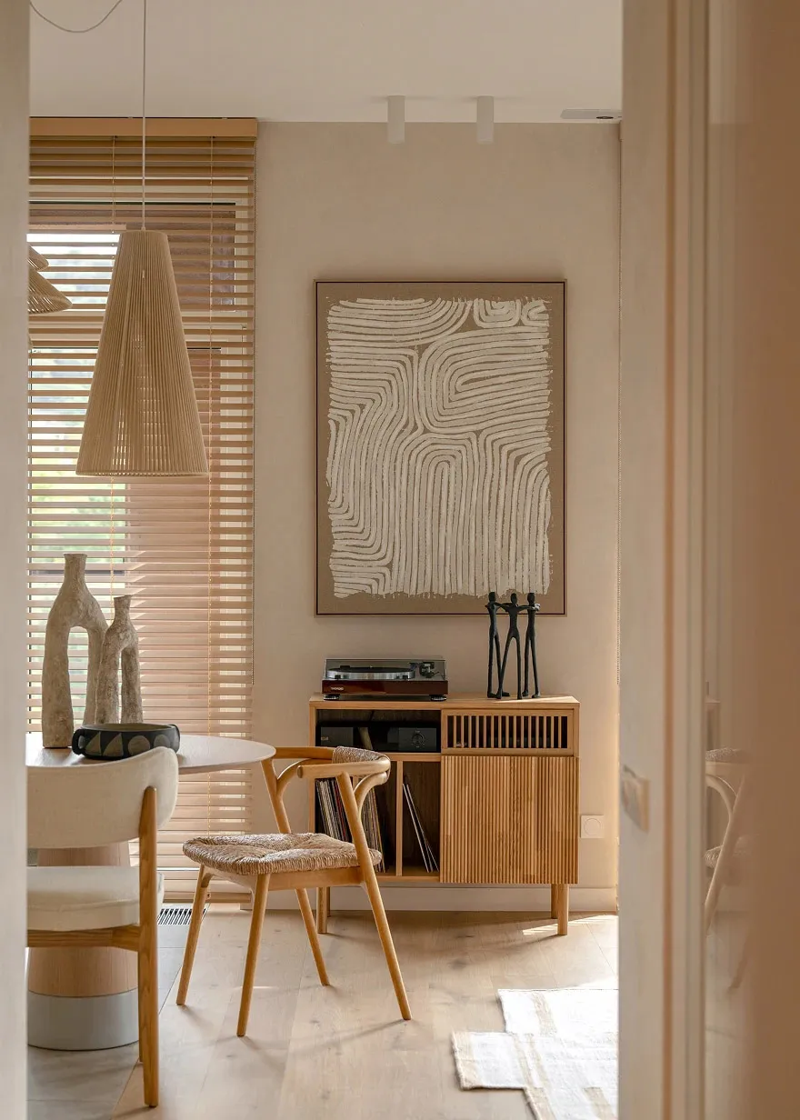A minimalist living room featuring wooden furniture, a pendant light, and abstract wall art.