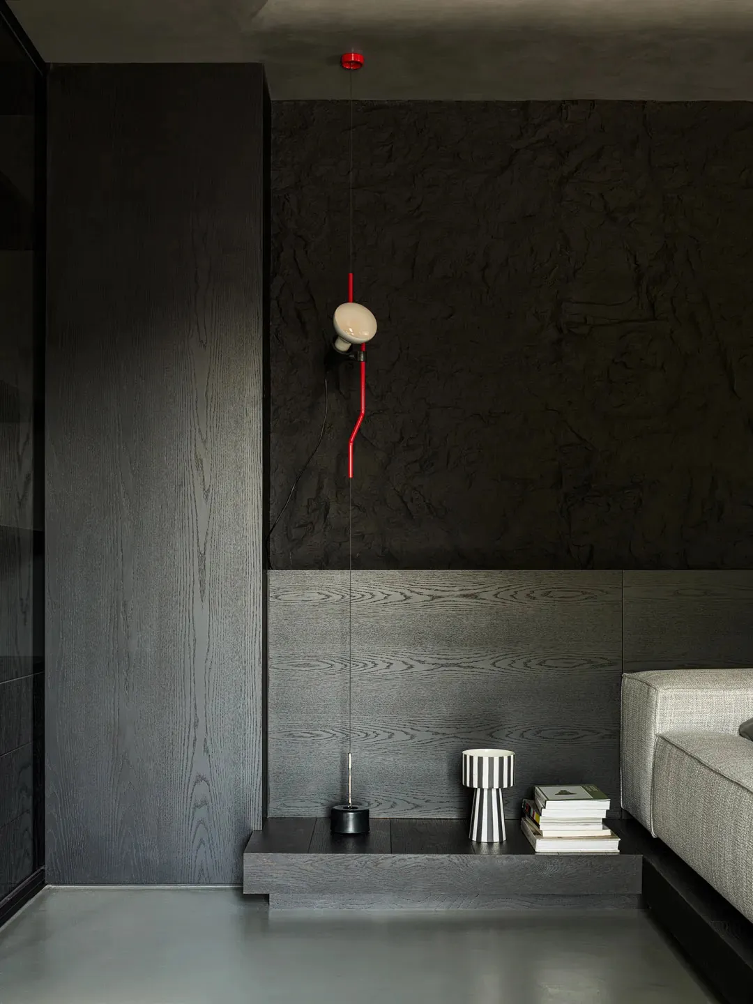A minimalist living room featuring dark wood walls, concrete flooring, and a gray sofa.