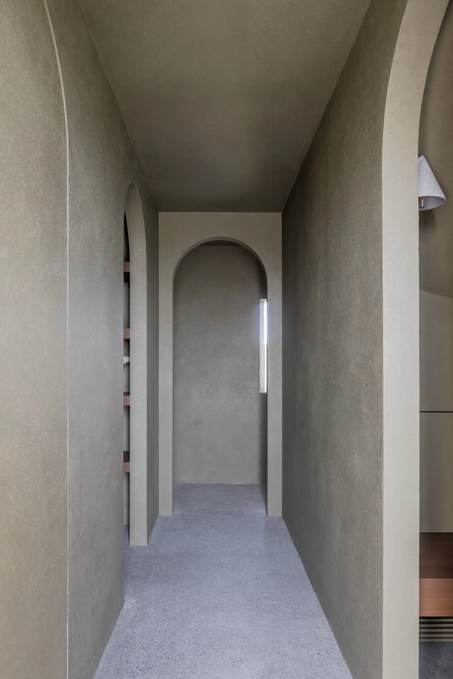Modern interior space featuring a minimalist design with concrete walls and a long hallway with arches and a skylight.