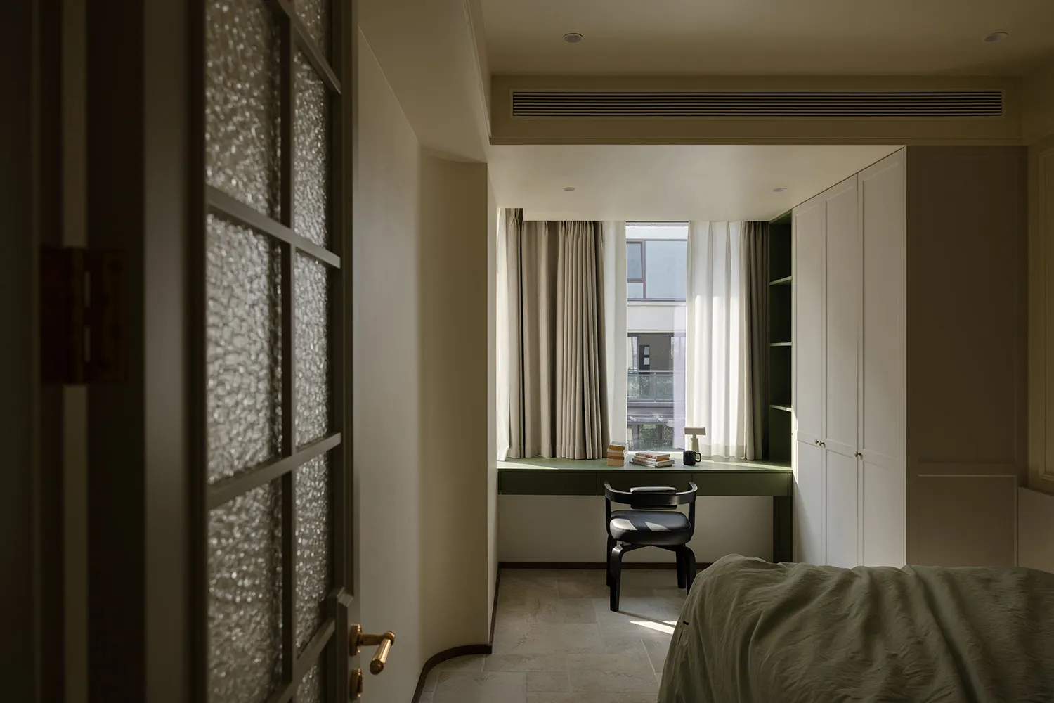 A modern minimalist bedroom featuring a window with curtains, a green desk, black chair, and a bed with a green blanket.
