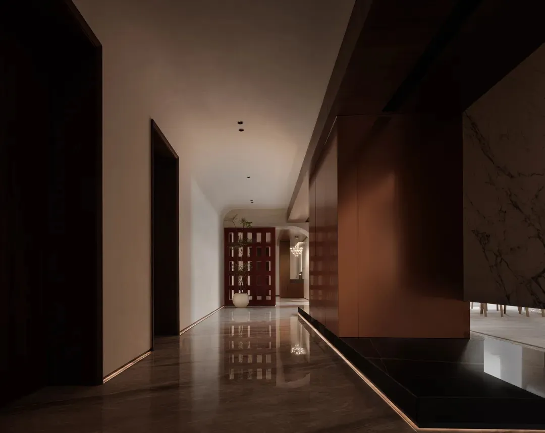 Modern minimalist entrance hallway with marble flooring and red wooden accents, featuring a potted plant and elegant lighting