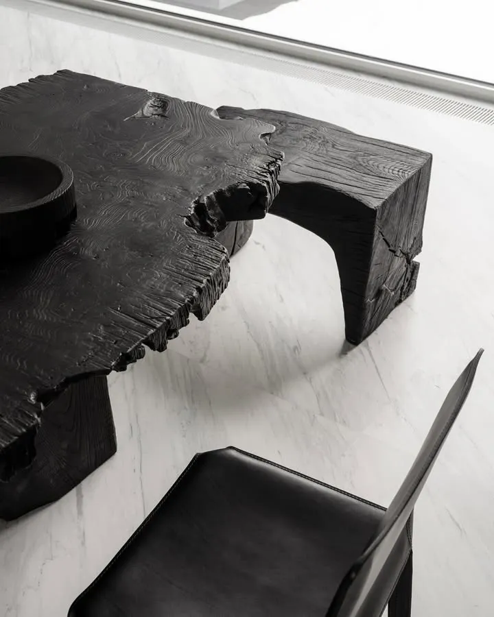 A modern, industrial-style black wooden table with a natural, raw finish.