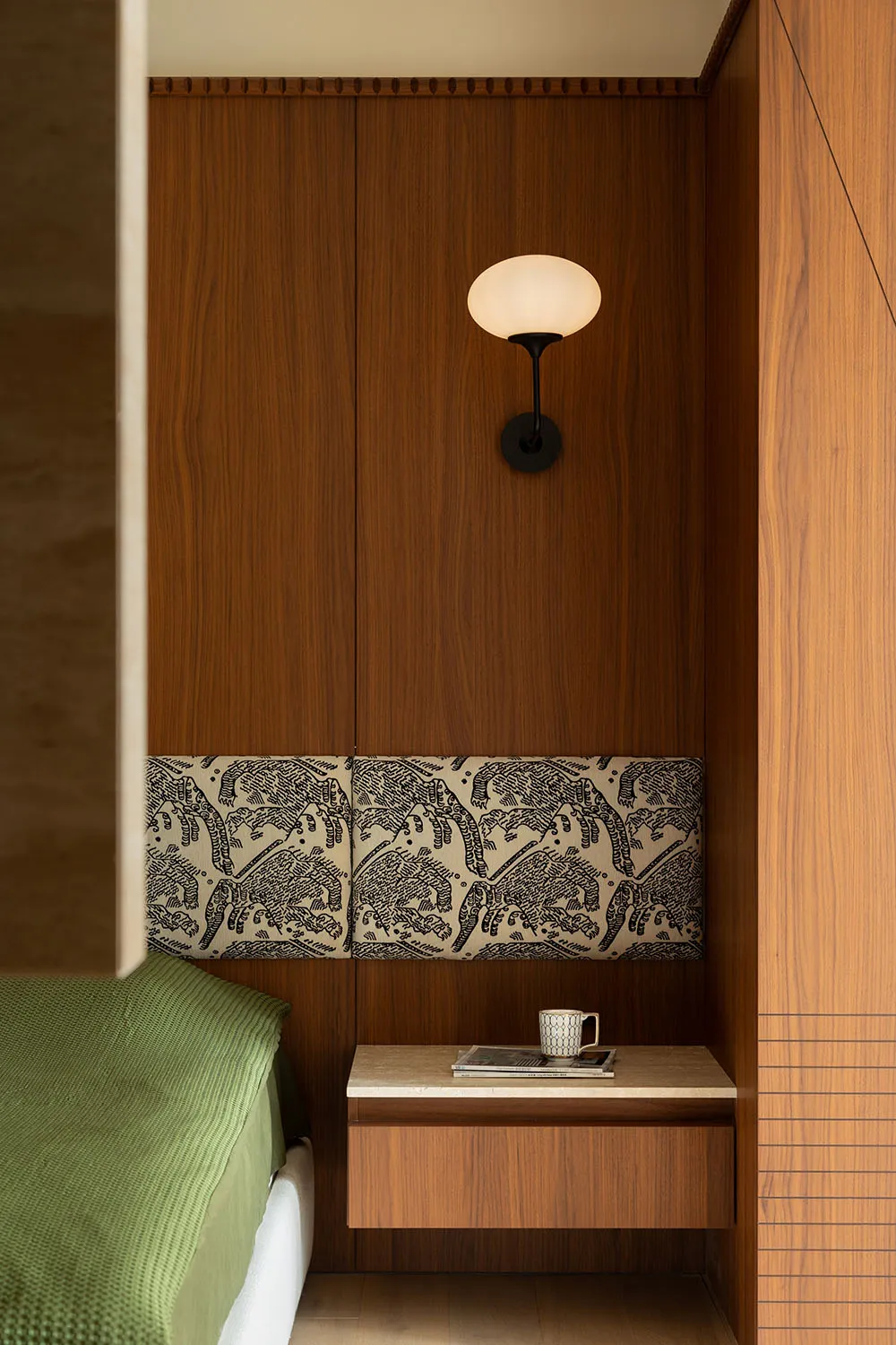 A minimalist bedroom features a floating wooden nightstand with a lamp and a cup and magazine on top.